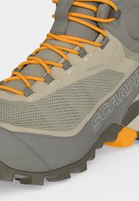 Κοντινό πλάνο μπεζ και γκρι παπουτσιού πεζοπορίας με πορτοκαλί κορδόνια, αναπνεύσιμο δίχτυ, ανθεκτική σόλα και την ένδειξη "SCARPA" στο πλάι.