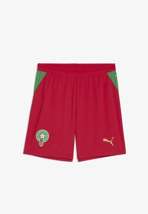 Czerwone krótkie spodenki sportowe z zielonymi bocznymi panelami, z złotym logo Puma i zielonym okrągłym emblematem z arabskim tekstem na lewym udzie.