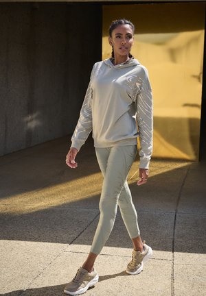 Light grey hooded sweatshirt with textured sleeves paired with light green leggings featuring a subtle pattern, completed with beige athletic shoes.