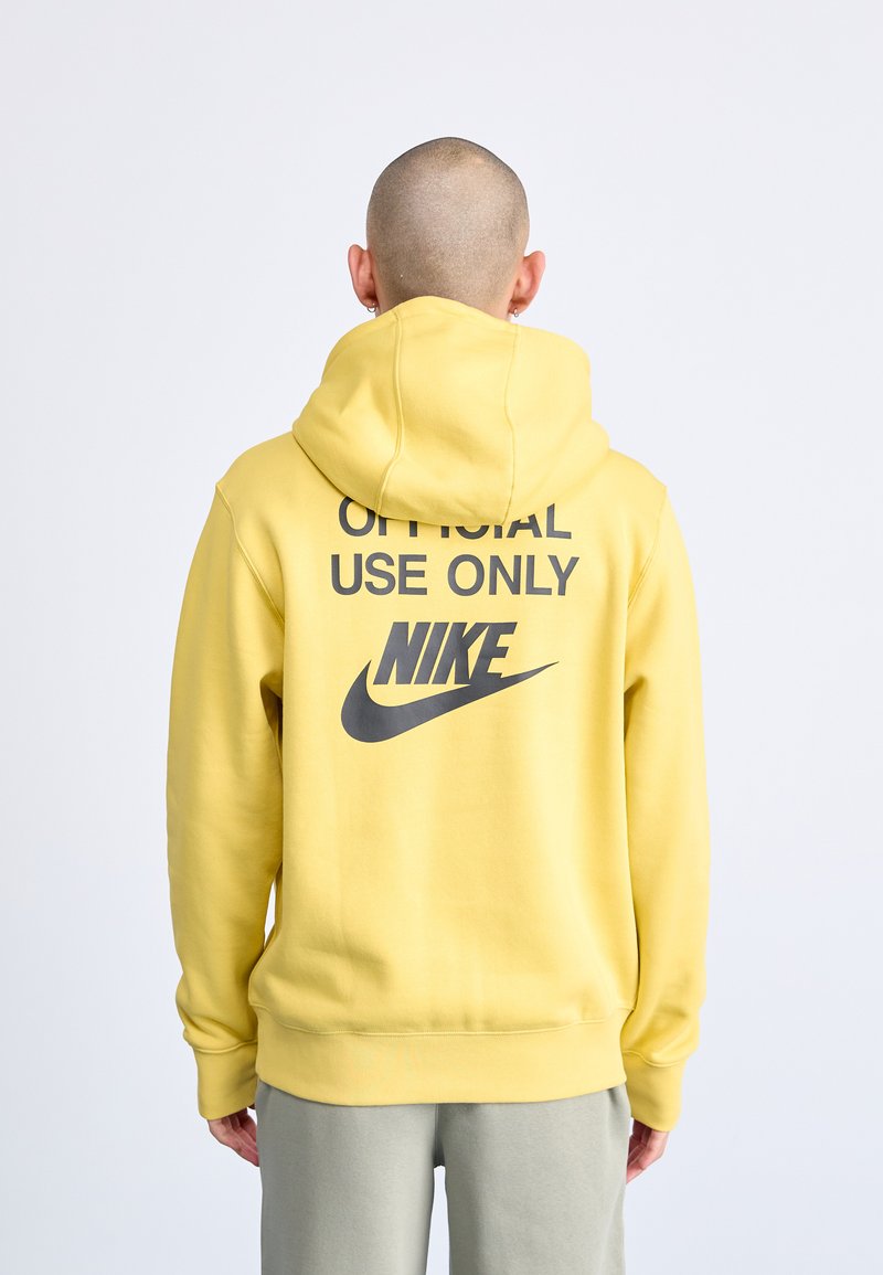 Sárga kapucnis pulóver, a hátsó oldalon fekete szöveggel: "CSAK HIVATALOS HASZNÁLATRA" és Nike logóval. Puha anyag, bordás mandzsettákkal és szegéllyel.