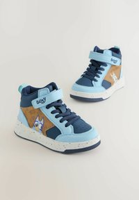 Zapatillas altas en azul claro y azul marino, con un panel marrón que presenta un gráfico de un personaje, suela de goma con detalles en blanco salpicado y correa ajustable.
