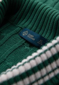 Suéter verde de punto con un patrón texturizado, cuello acanalado y una etiqueta de tela que muestra "Ombre Heritage", talla M y 48 EUR.