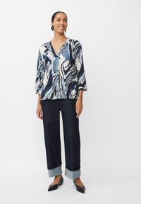 Blusa casual a maniche tre quarti e vestibilità ampia con un motivo a marmo blu navy, bianco e verde acqua. Abbinata a jeans scuri con risvolti alla caviglia e ballerine nere.