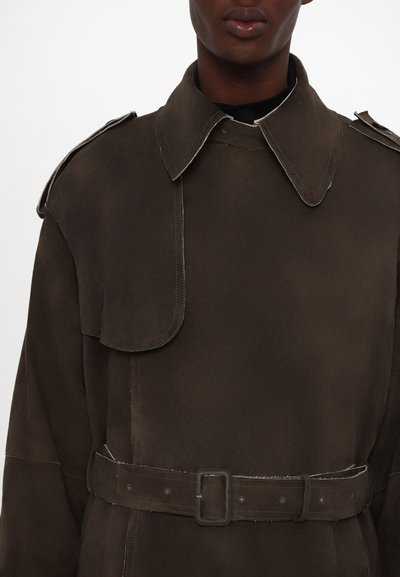 Khakifarbener Trenchcoat mit einem großen Kragen, Schulterklappen und tailliertem Gürtel. Besitzt einen glatten, strukturierten Stoff und sichtbare Nähdetails.