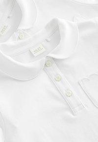 Weiße Poloshirts aus Baumwolle mit klassischem Kragen, featuring Knopfverschluss und dezente gestickte Herzdetails auf einem Shirt.