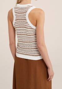 Stickad ärmlös topp med vita och bruna horisontella ränder. Texturerad garn och ribbad nederkant ger ett lager-på-lager utseende. Slät finish.