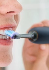 Brosse à dents électrique avec un manche noir et une tête de brosse bleu clair. Mise au point sur les dents, montrant une apparence propre et soignée.