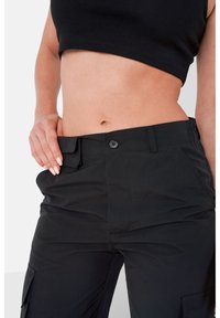 Pantaloni cargo neri con una texture liscia e opaca, dotati di chiusura a bottone, tasche laterali e una vestibilità comoda sui fianchi e la vita.