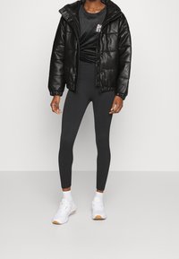 Doudoune noire brillante, leggings noirs ajustés et baskets blanches avec des accents orange, portées sur un haut noir.