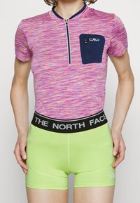 Haut à manches courtes, rose et violet avec un motif, doté d'un col zippé et d'une poche marine, associé à un short taille haute vert citron avec une bande logo noire.