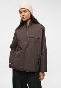 Rjav, lahek pulover s četrtinastim zadrgo in žepom na prsih ter stranskima žepoma z zadrgo. Mehka tekstura in sproščen fit.