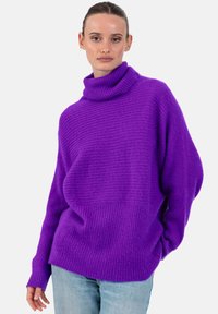 Pull violet en maille côtelée avec un col montant, une coupe ample et des manches longues. Présente une texture horizontale et une silhouette décontractée.