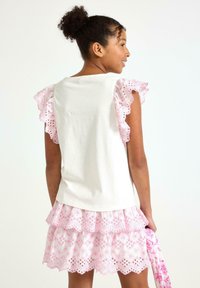 Hvid bomuldsbluse med pink volangærmer, parret med en pink eyelit blonde, lagdelt nederdel med blomster mønstre og udskæringer.