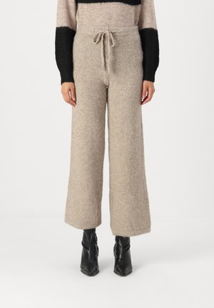Beige strikkede brede bukser med snor i taljen, tekstureret stof og en blød finish. Kombineret med sorte ankelstøvler.