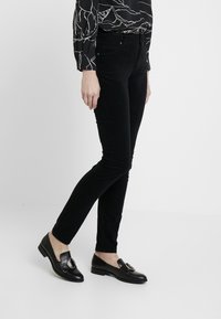 Černé kordové skinny kalhoty s jemnou texturou, zkombinované s černými mokasíny s kulatým kovovým akcentem.