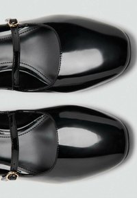 Pantofi Mary Jane din piele lac neagră, cu vârf rotund, având o curea subțire peste gheată și o cataramă de culoare aurie.