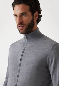 Maglione grigio con zip e colletto alto, realizzato in morbido tessuto testurizzato. Presenta una cerniera argentata e un design aderente per un aspetto snello.