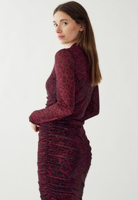 Czarna sukienka w cętki, w kolorze czerwonym i czarnym, z długim rękawem, z marszczeniami po bokach, które dodają tekstury i podkreślają sylwetkę.