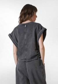 Šedý, oversize pulovr s širokými rukávy a švem na zadní straně. Vyrobeno z měkké látky s vybledlou texturou a minimálním označením značky.