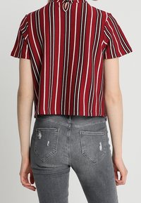 Blusa de tirantes cortos a rayas rojas y blancas con detalle de apertura en la parte de atrás, combinada con jeans ajustados grises desgastados.