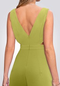 Groene jumpsuit met een diepe V-achtige rug, uitsnijdingen aan de zijkanten en een nauwsluitende taille. Gladde textuur met een verborgen ritsdetail aan de achterkant.