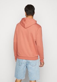 Ljus korallfärgad hoodie med dragsko, ribbade manschetter och nederkant; matchad med blå denimshorts med fransar och fickor.