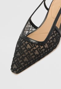 Chaussure slingback noire à bout pointu avec mesh transparent et motif géométrique texturé, semelle intérieure rembourrée beige et bordure en cuir.