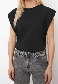 Sort kortærmet top med polstrede skuldrer, parret med højtaljede, falmede sorte jeans med knaplukning og forlommer.