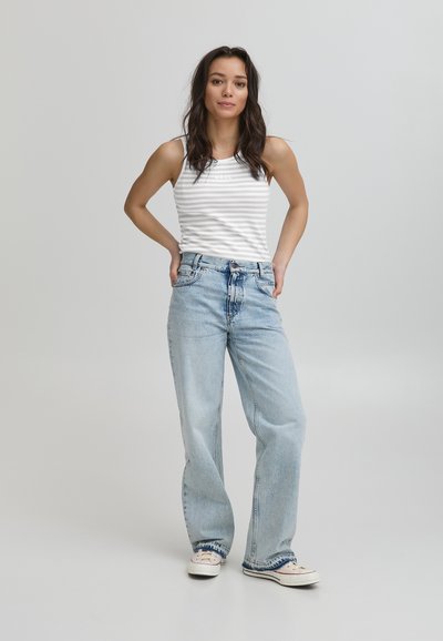 Jasnoniebieskie dżinsy w szerokim kroju, luźne, zestawione z białą bluzką na ramiączkach w paski. Strój uzupełniają casualowe białe sneakersy.