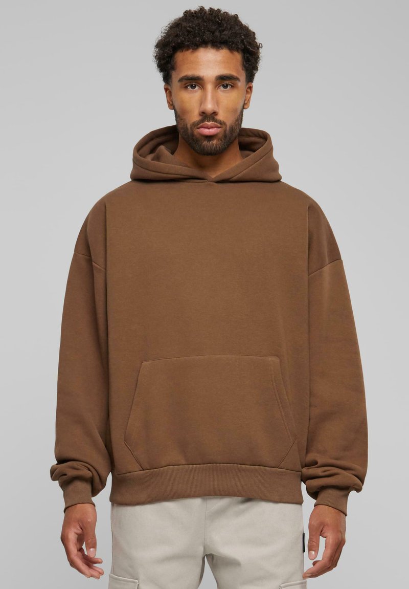 Hoodie en coton marron avec une poche avant, des ourlets et des poignets côtelés, et une capuche doublée. Présente une coupe décontractée et des coutures d'épaule tombantes.