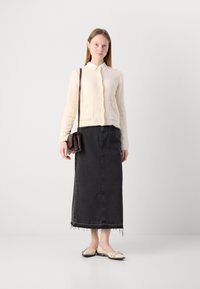 Beige texturerad kardigan med framfickor, kombinerad med en svart denim maxi kjol med fransat nederkant, och krämfärgade ballerinas med slinga.