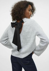 Maglione grigio con un taglio sulla schiena che presenta un grande fiocco in satin nero. Tessuto morbido, maniche ampie e una vestibilità comoda. Abbinato a jeans scuri.