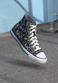 Leopardenmuster-Hochschuh-Sneaker mit einem Obermaterial aus Canvas, weißen Schnürsenkeln und einer Gummisole mit einer weißen Zehenkappe, die über einer strukturierten Oberfläche schwebt.