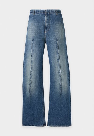 Τζιν denim μπλε με ψηλή μέση, φαρδιά μπατζάκια, έντονες μπροστινές ραφές, ξεθωριασμένο ξέπλυμα και χωρίς ορατές τσέπες, σε λευκό φόντο.