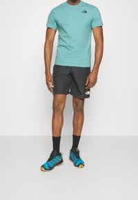 Tyrkysové bavlněné tričko, černé sportovní šortky a modré běžecké boty s černými akcenty. Výrazné logo na tričku a šortkách. Texturovaná tkanina.