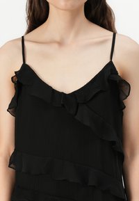 Haut sans manches noir avec un décolleté en V et des accents froncés sur le devant, en tissu texturé avec une finition légèrement froissée.