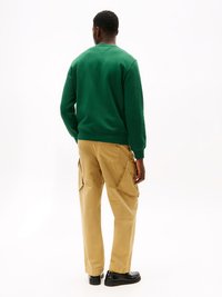 Πρ�άσινη μπλούζα φούτερ με ελαστικές μανσέτες και στρίφωμα, συνδυασμένη με χακί παντελόνια cargo που διαθέτουν πολλές τσέπες και χαλαρή εφαρμογή, φορεμένα με μαύρα παπούτσια.