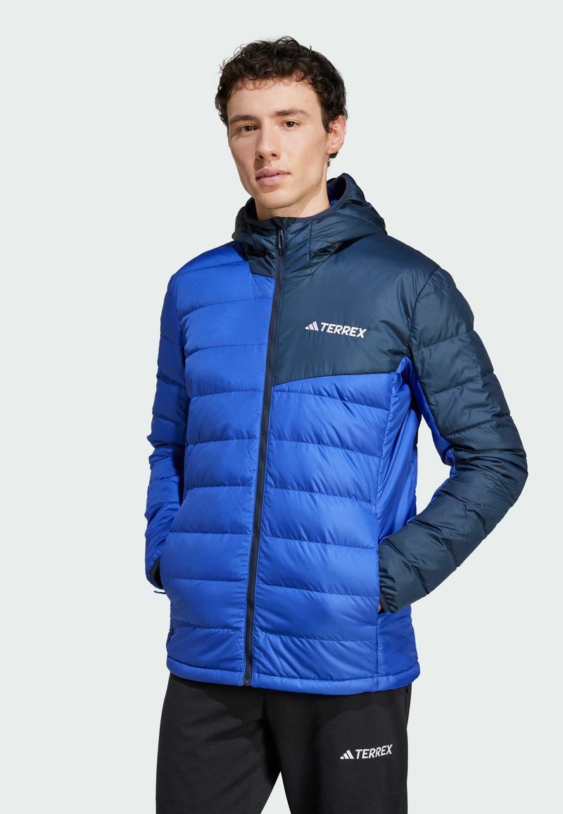 Blå puffjacka med quiltad design, mörkblå huva och logotyp på bröstet. Har full dragkedja och sidofickor. Mjukt material och konstruktion.