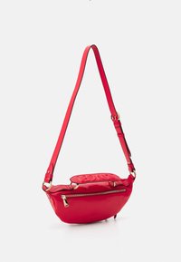 Sac à bandoulière en cuir rouge avec une forme incurvée, doté d'une poche zippée à l'avant et d'une sangle réglable. Logo embossé sur le rabat supérieur.