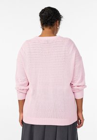Nadrozmerný ružový sveter vyrobený zo softového úpletu, s rebrovanými manžetami a lemom, so štruktúrovanými detailmi na rukávoch.