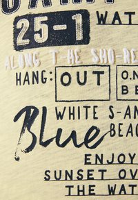 Tela de color amarillo claro con texto en blanco y negro que incluye frases como "Playa Azul", "Disfruta del Atardecer" y letras decorativas. Incluye detalles texturizados.