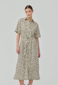 Vestido midi em tecido bege com padrão floral preto, mangas curtas, frente com botões e detalhe de cintura laçada.
