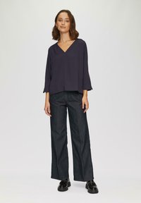 Marineblaue, locker sitzende Bluse mit V-Ausschnitt und dreiviertellangen Ärmeln, kombiniert mit dunklen, weiten Hosen und schwarzen Schuhen. Textil mit Struktur.
