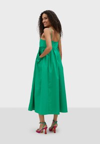 Grön bomullsmaxikjol med spagettiband, rynkad midja och sidan fickor. Stylad med flerfärgade klacksandaler.