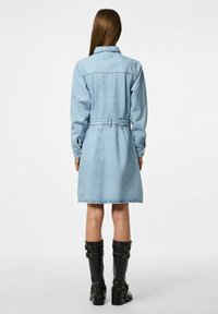 Light blue denim dress with long sleeves, button closure, belted waist, and a mid-length skirt. Worn with black knee-high boots.