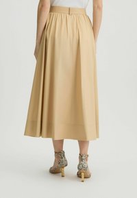 Gonna midi beige con vita arricciata, texture liscia e un leggero sheen. Abbinata a sandali con tacco in stampa rettile beige con dettagli dorati.