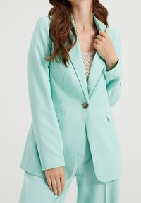 Světlá mátově zelená sako z hladkého materiálu, zapínání na jeden knoflík, klopové límce, dvě boční kapsy, přiléhavý střih, v kombinaci s pleteným topem.