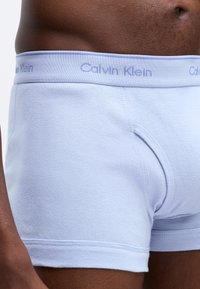 Boxer briefs in cotone azzurro chiaro con una morbida cintura elastica che presenta il logo "Calvin Klein" in lilla chiaro. Design aderente con una texture liscia.