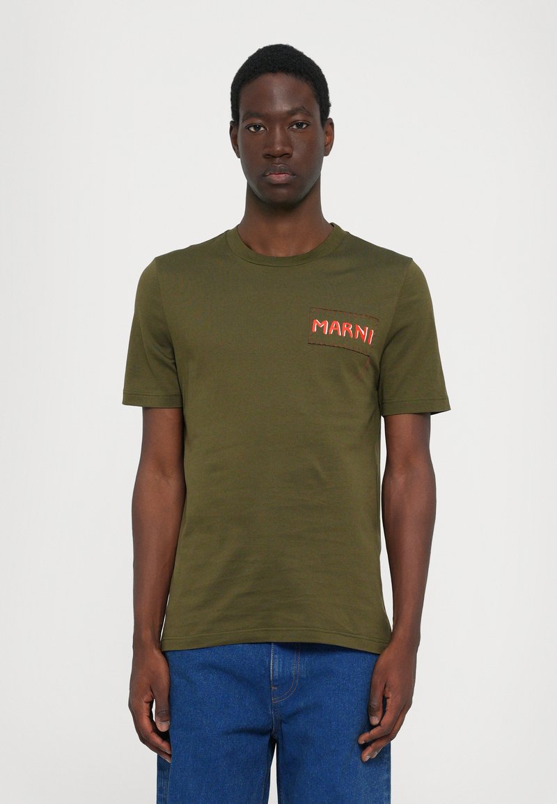 Tricou din bumbac verde măsliniu, cu guler rotund și mâneci scurte, având un patch brodat roșu cu logo pe piept.
