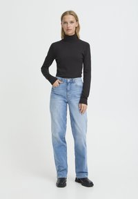 Haut noir à col roulé, manches longues ; jean en denim bleu clair, taille haute, coupe droite ; porté avec des bottines noires ; style minimaliste.